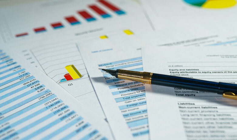 Charts and graphs on a desk under a pen