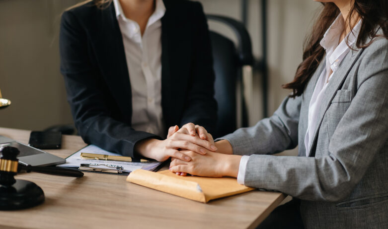 two women sitting with clasped hands over documents